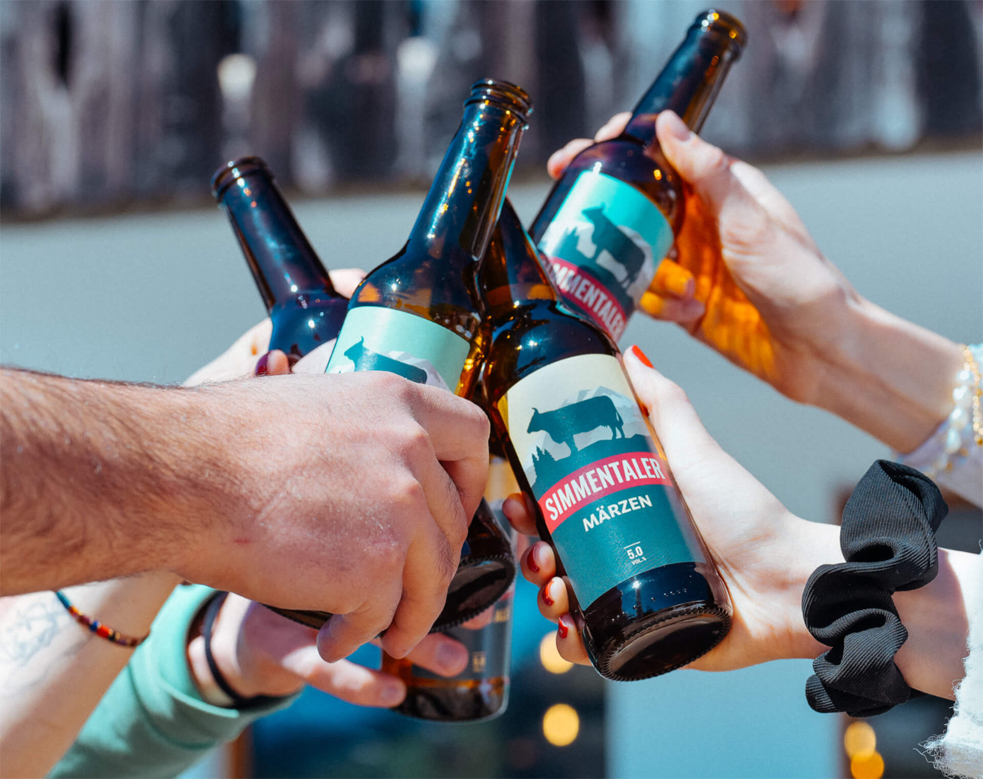 Hände von Leuten die mit Simmentaler Bier Flaschen anstossen.