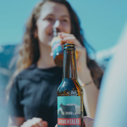 Frau welche in Gesellschaft an einem Simmentaler Bier nippt.